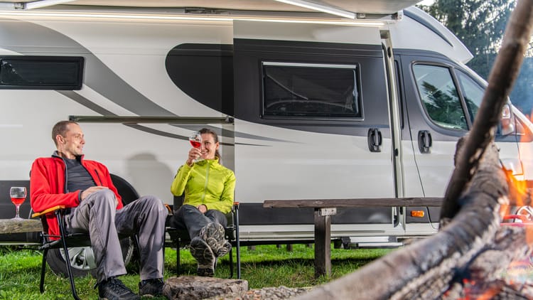 a couple boondocking without hookups in their rv in the woods near a campfire drinking wine